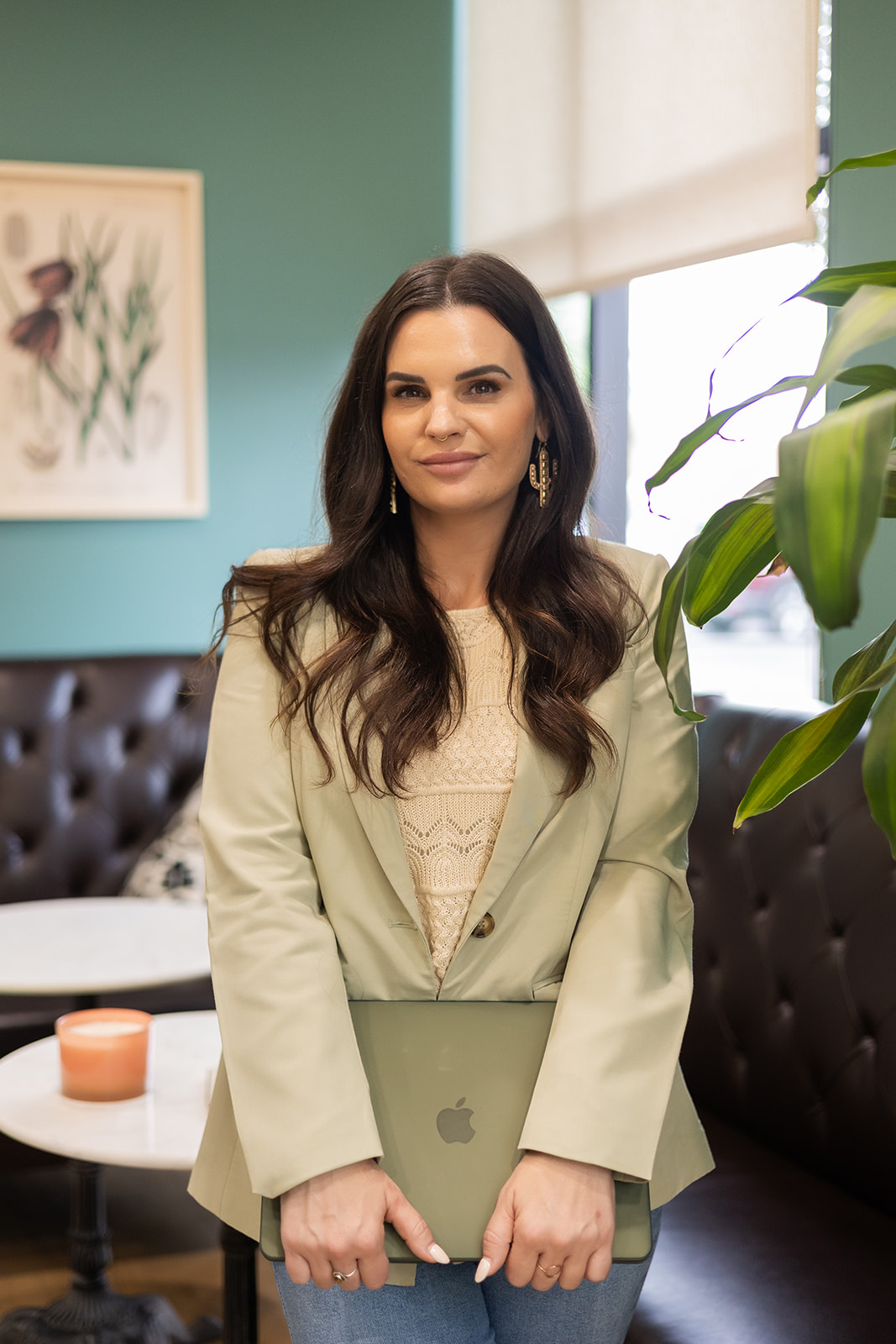 Therapist in Gilbert, Arizona specializing in emotional overwhelm and mental health after leaving church, standing with laptop in welcoming office space with plants and artwork